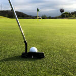 A golf club poised to putt a golf ball across the green